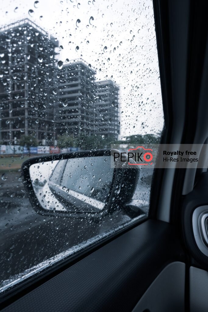 Rain shower view from inside car with side mirror in frame and water droplets on side window