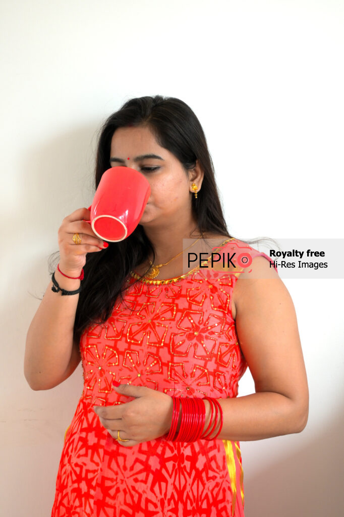 
									Beautiful Indian model in vibrant red suit posing with red mug of tea