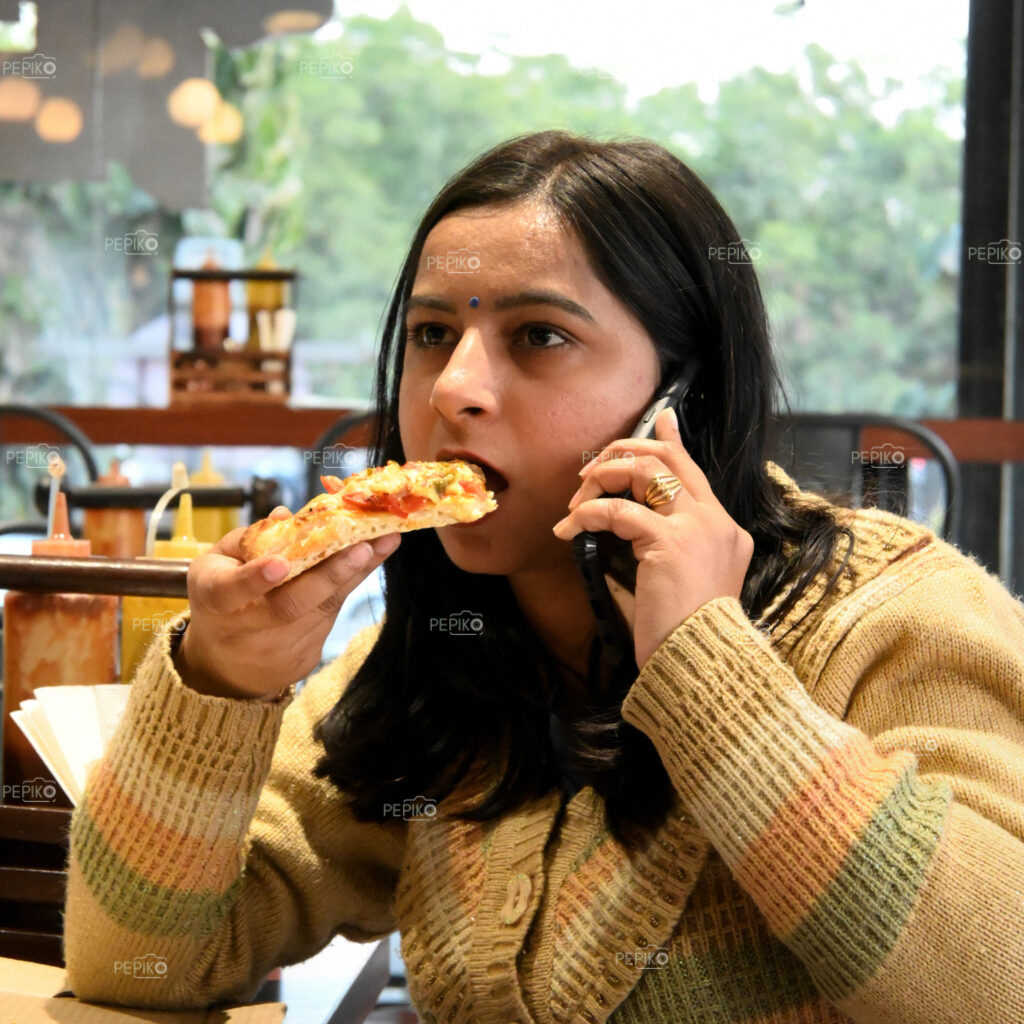 Women enjoying her slice of pizza and phone / cell phone in her other hand
