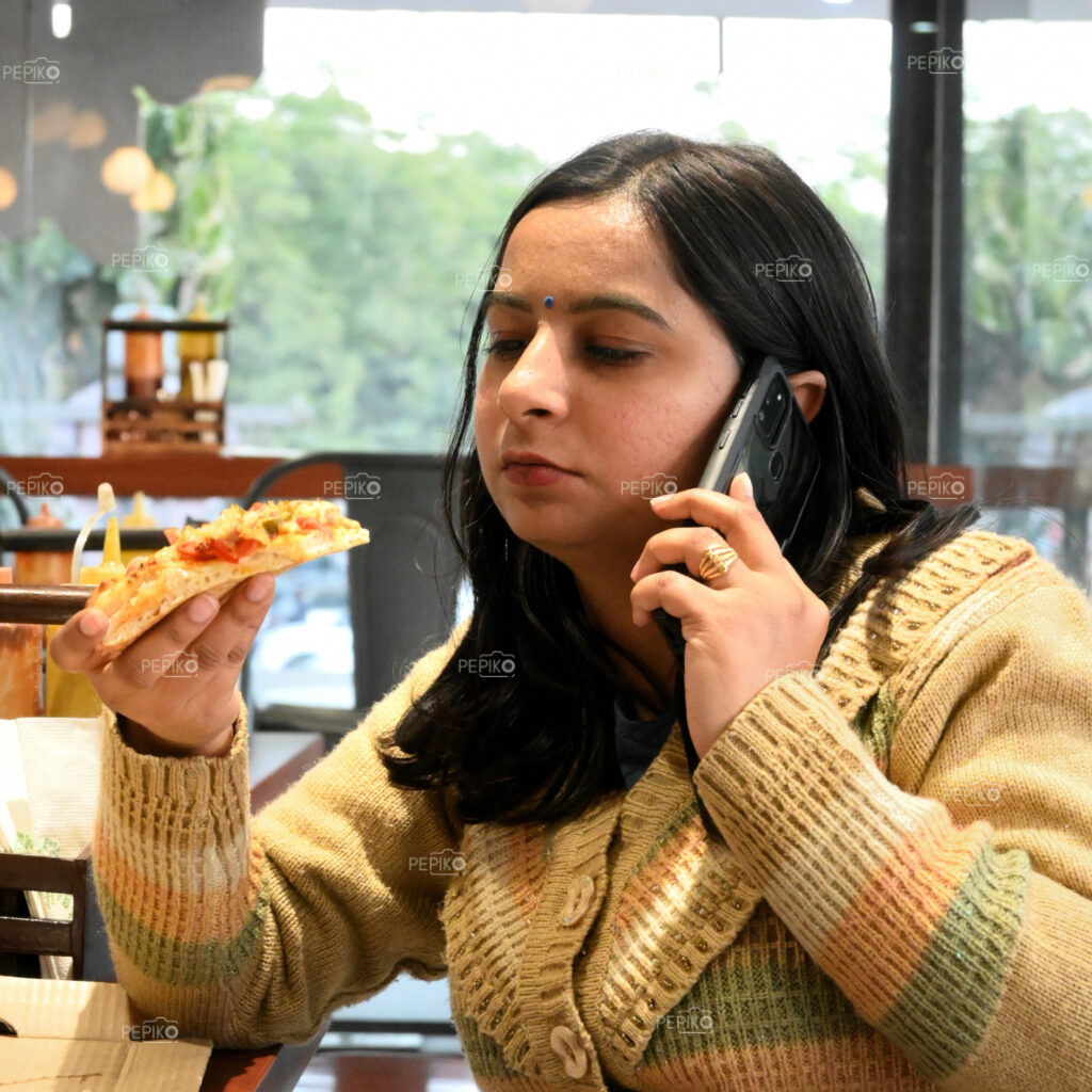 Indian girl eating pizza while talking on phone / cell phone