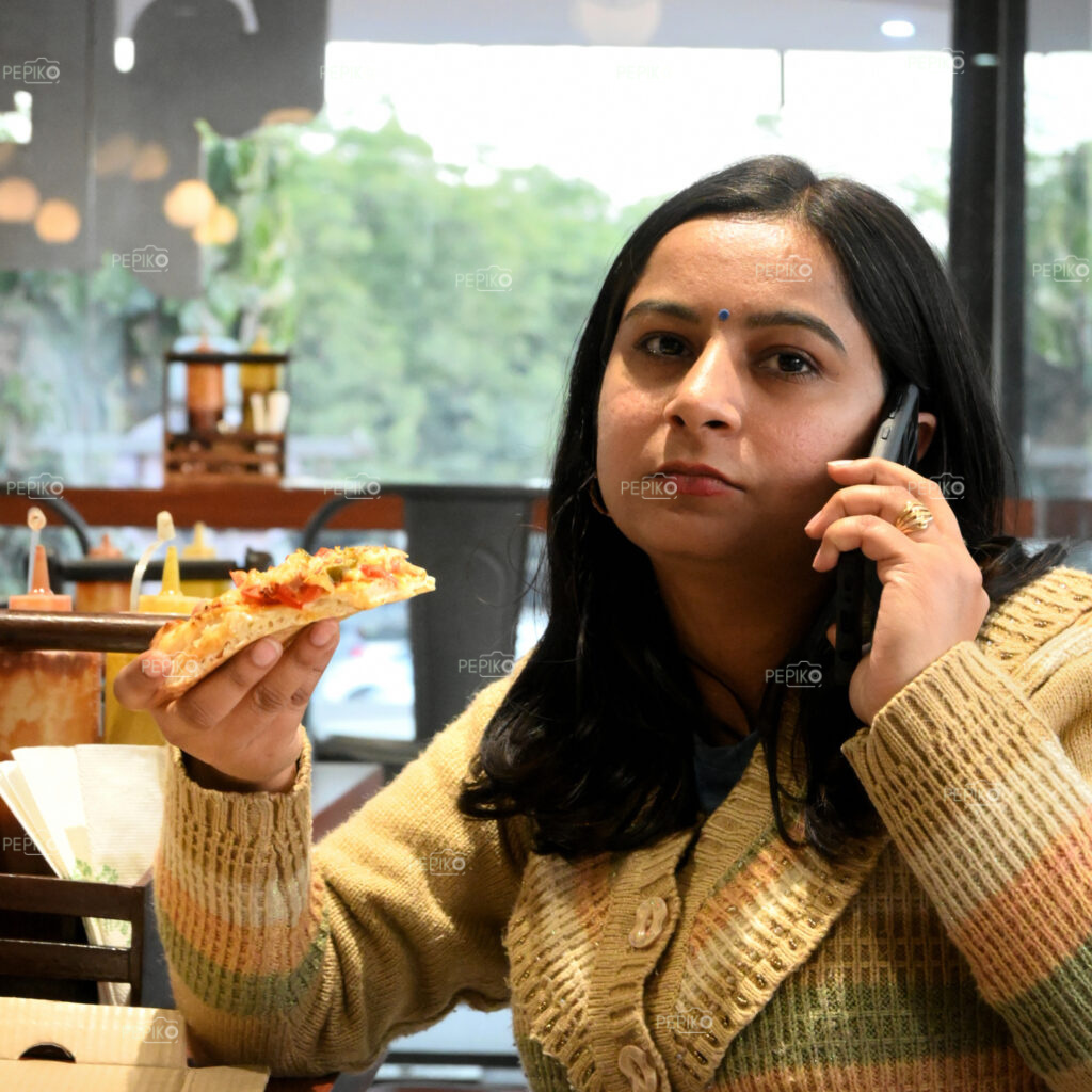 Girl having conversation on cell phone / mobile phone while eating pizza